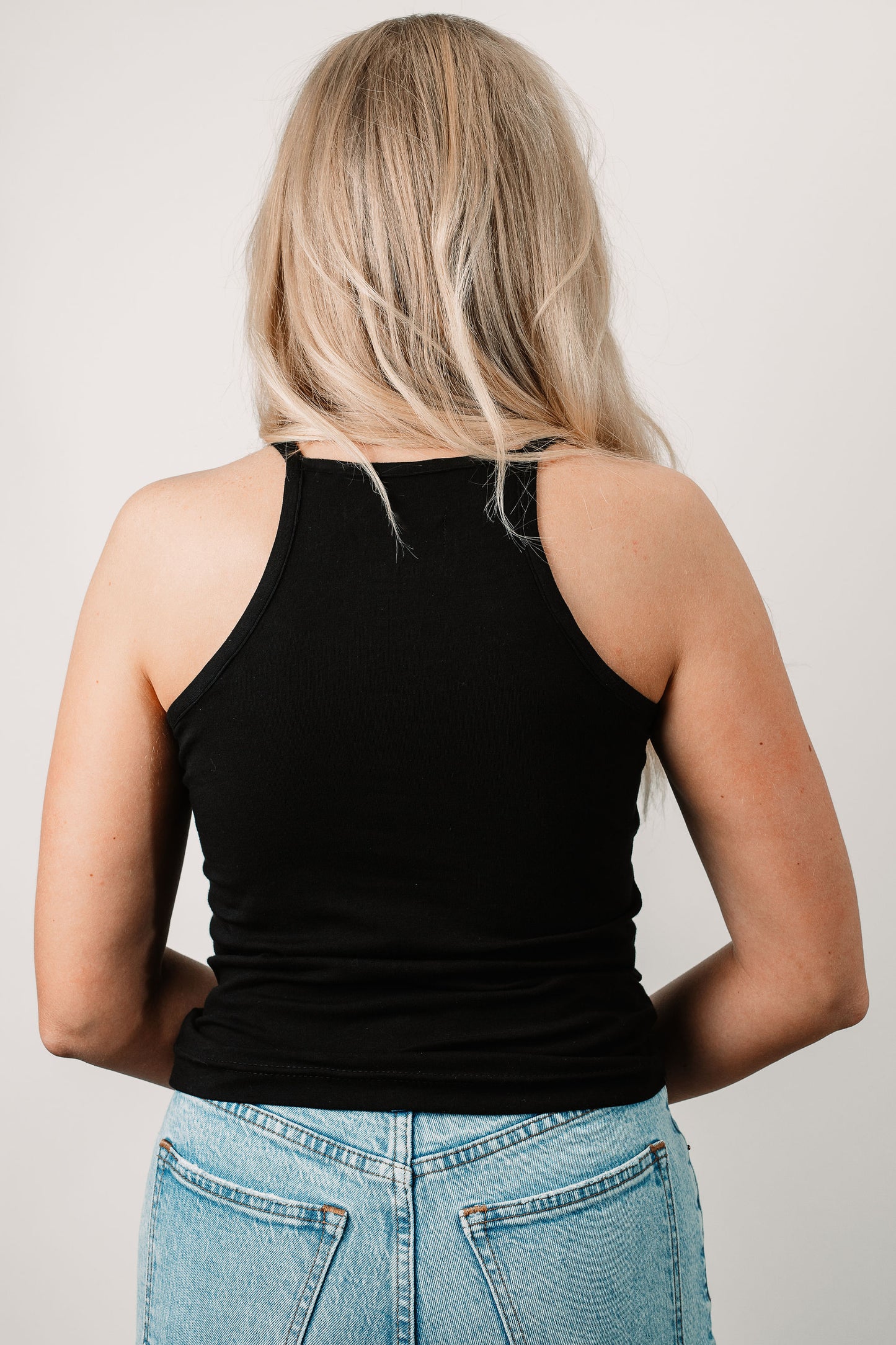 Charlotte wears the Willa High Neck Tank in Black in size XS. Back view.