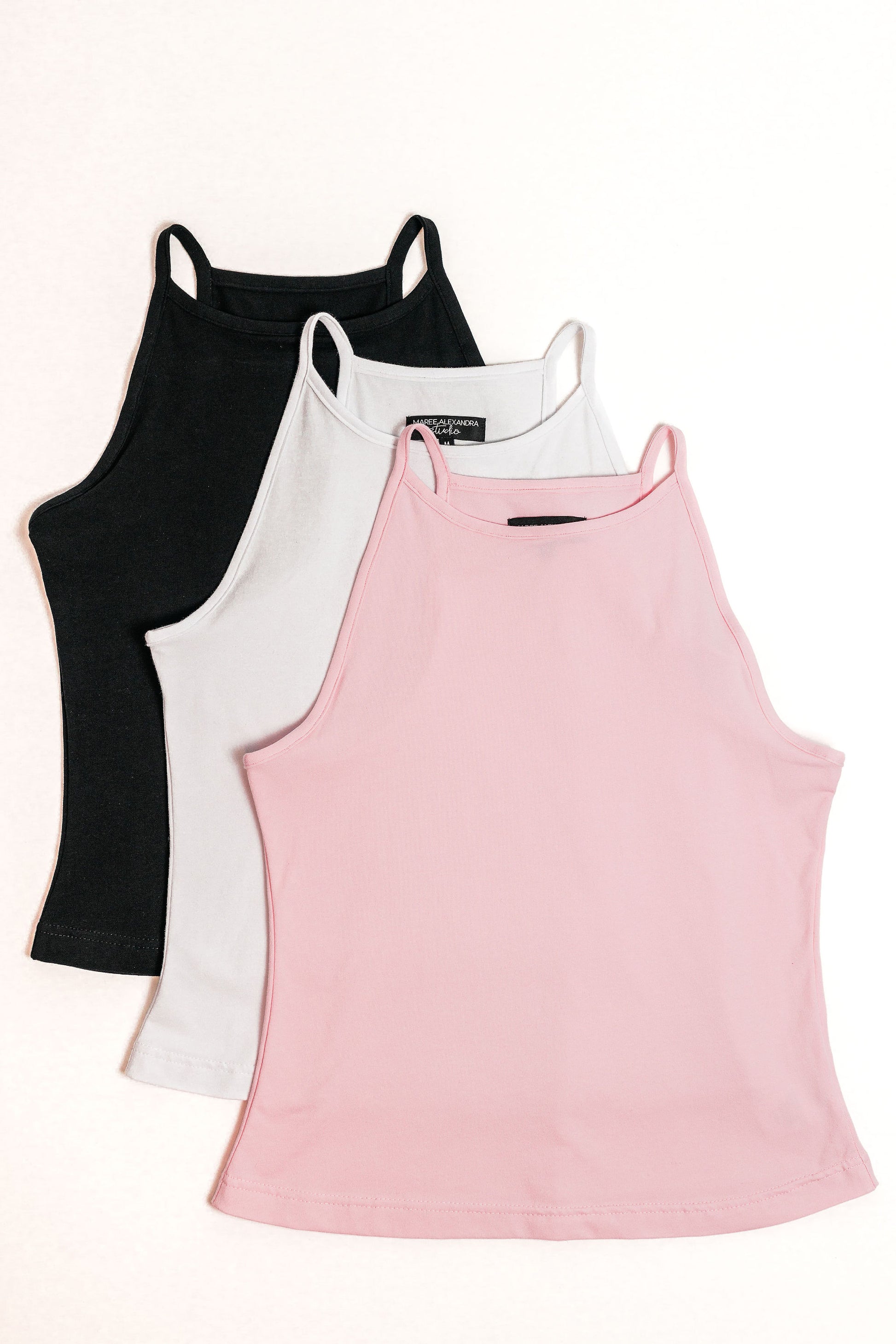 Flat lay of the Willa High Neck Tank Top. It shows three colours, Baby Pink, White, and Black.