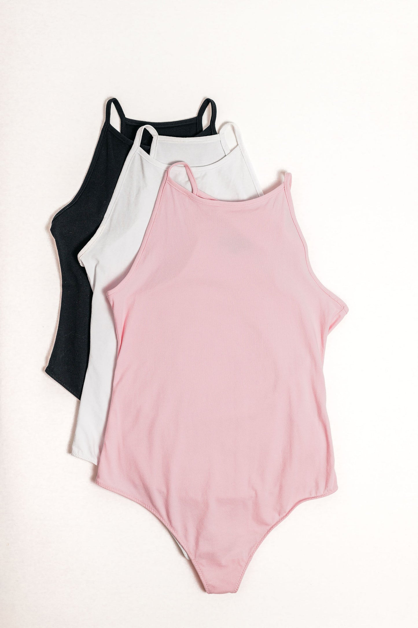 Flatlay of the Willa Bodysuits in all three colours. Baby Pink, White and Black.
