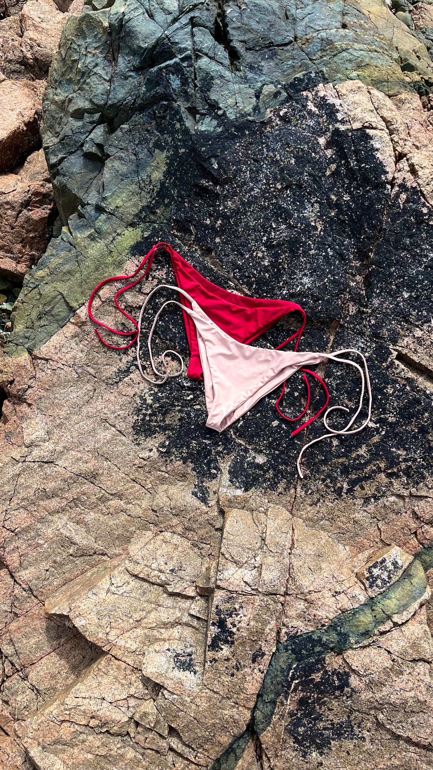 The Bella Bikini Bottoms laying on the rock in Crimson and Sand.