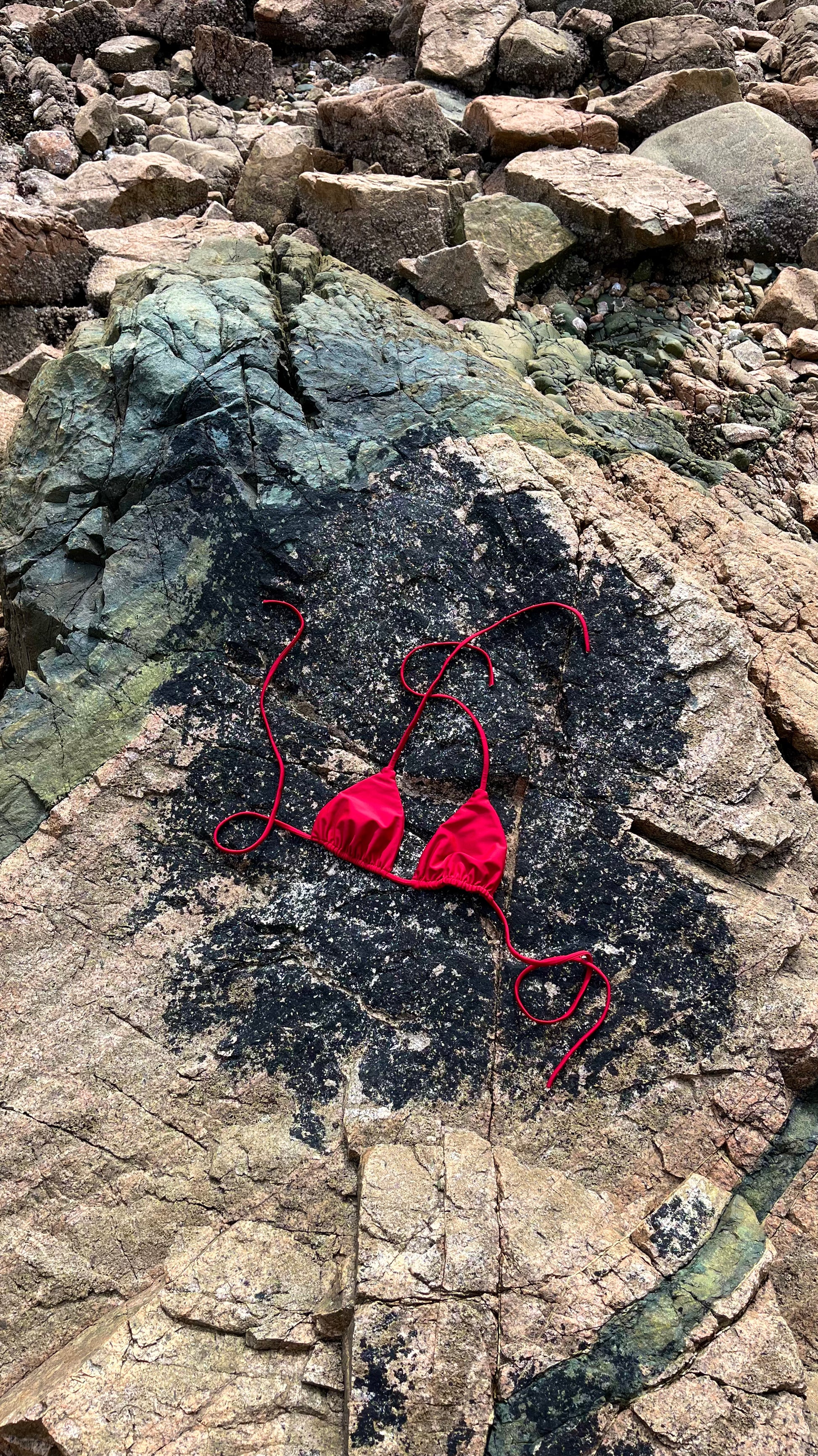 The Bella Bikini Top laid on the rock in Crimson.