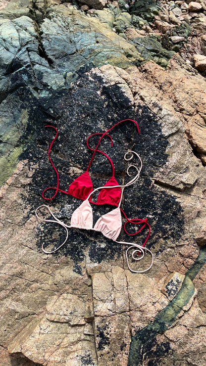 The Bella Bikini Top laid on the rock in 2 colours (Crimson and Sand).