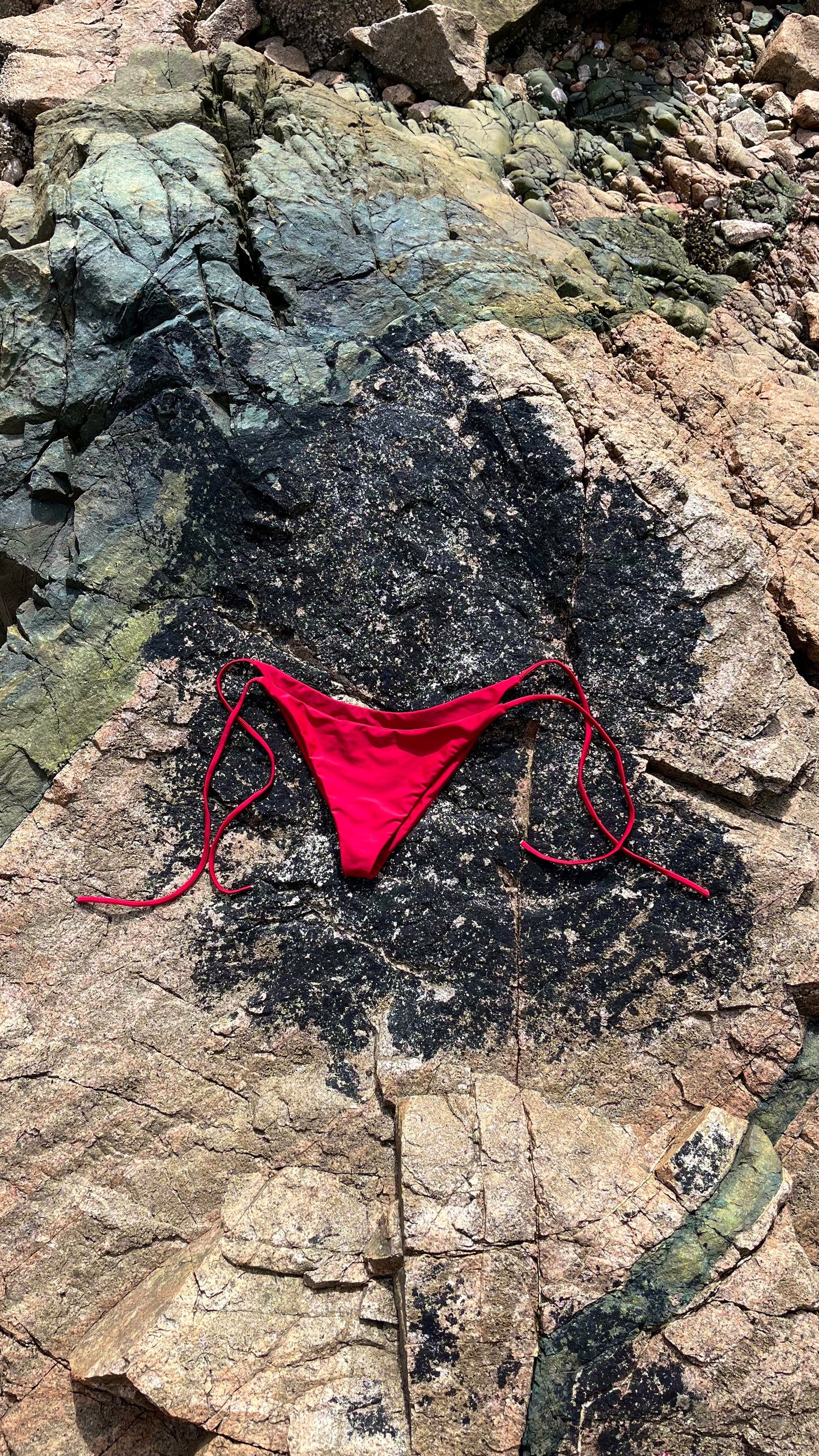 The Bella Bikini Bottoms laying on the rock in Crimson.