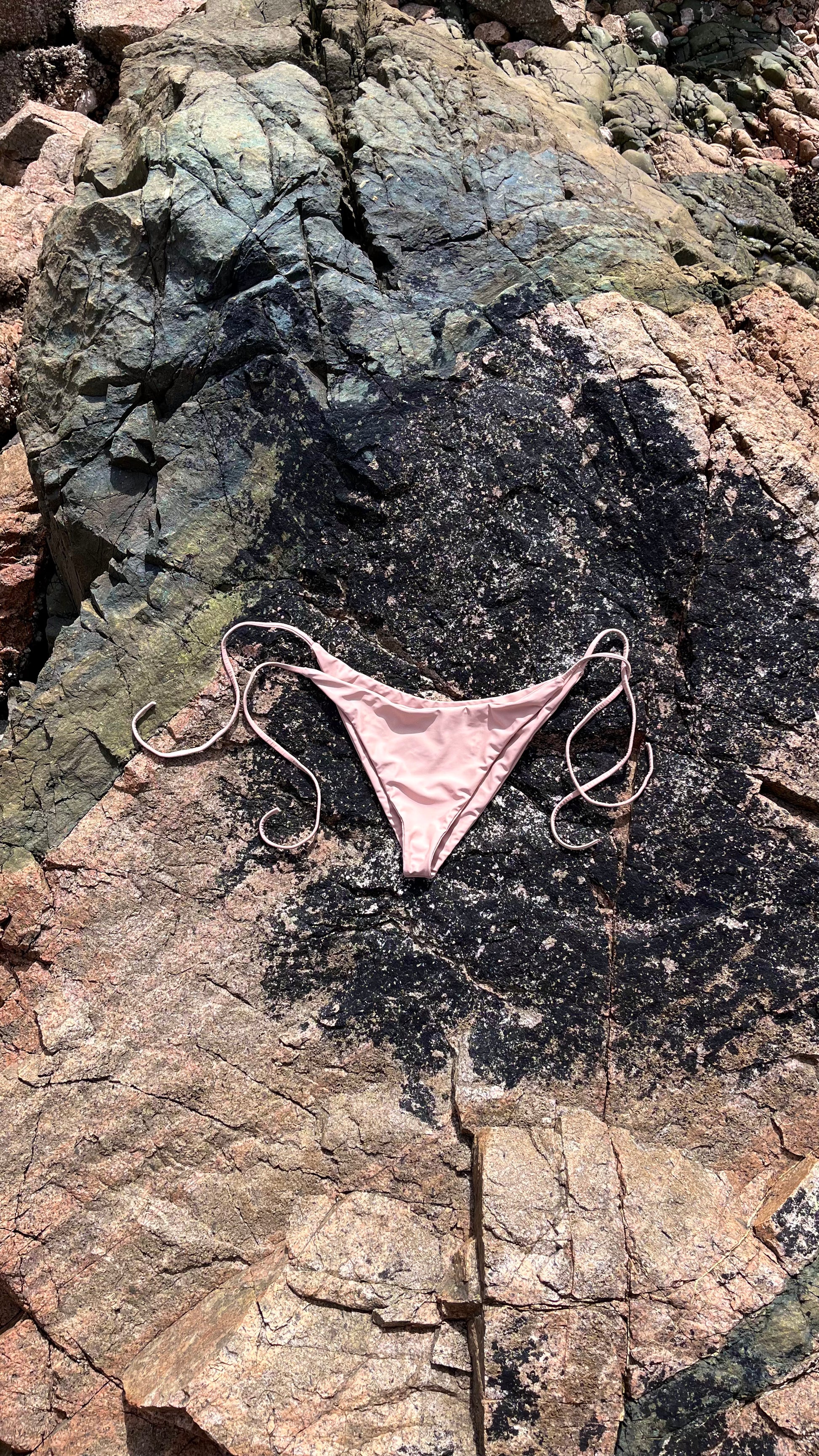 The Bella Bikini Bottoms laying on the rock in Sand.